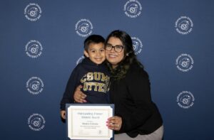 Bianca Estrada and her son smile at the camera while holding an "Outstanding future Alumni" Award