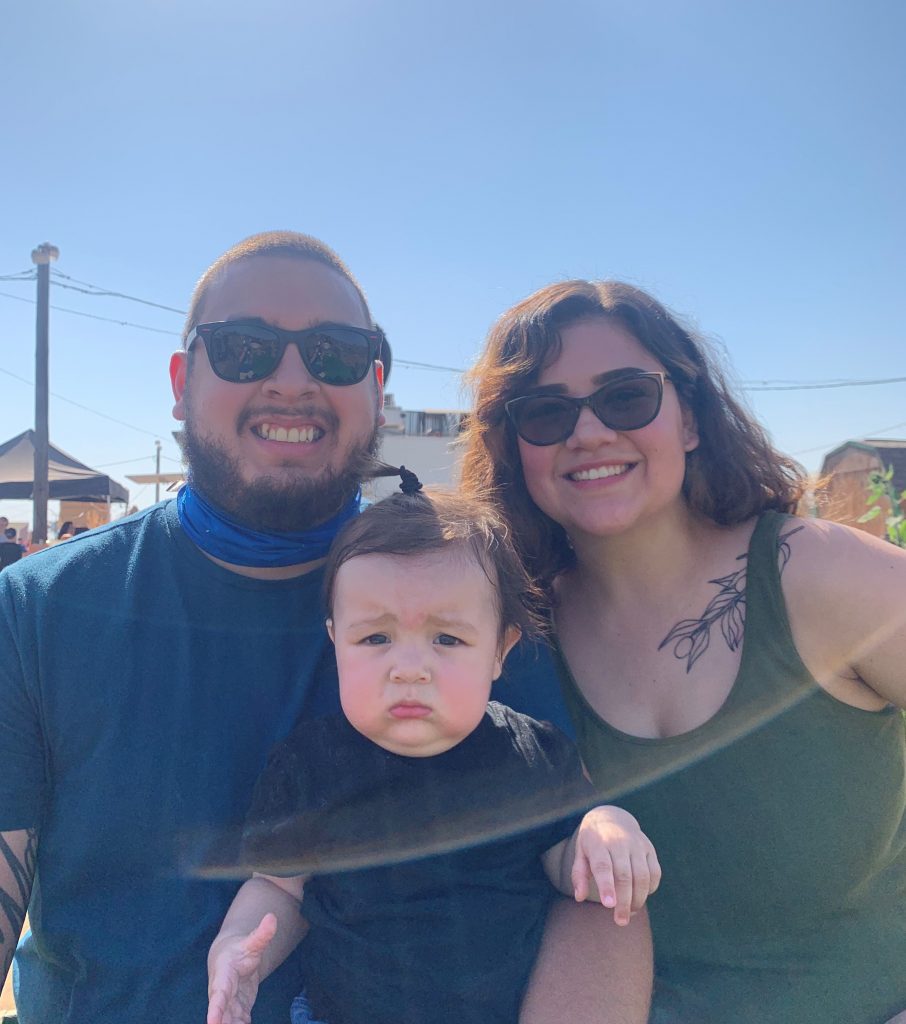 Marcella, baby and husband smiling at the camera